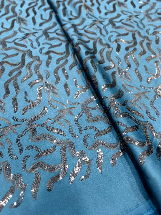 Azure blue TR satin fabric with heavy silver sequin embroidery in abstract flowing patterns, ideal for koti, blazer and Indo-western outfits.