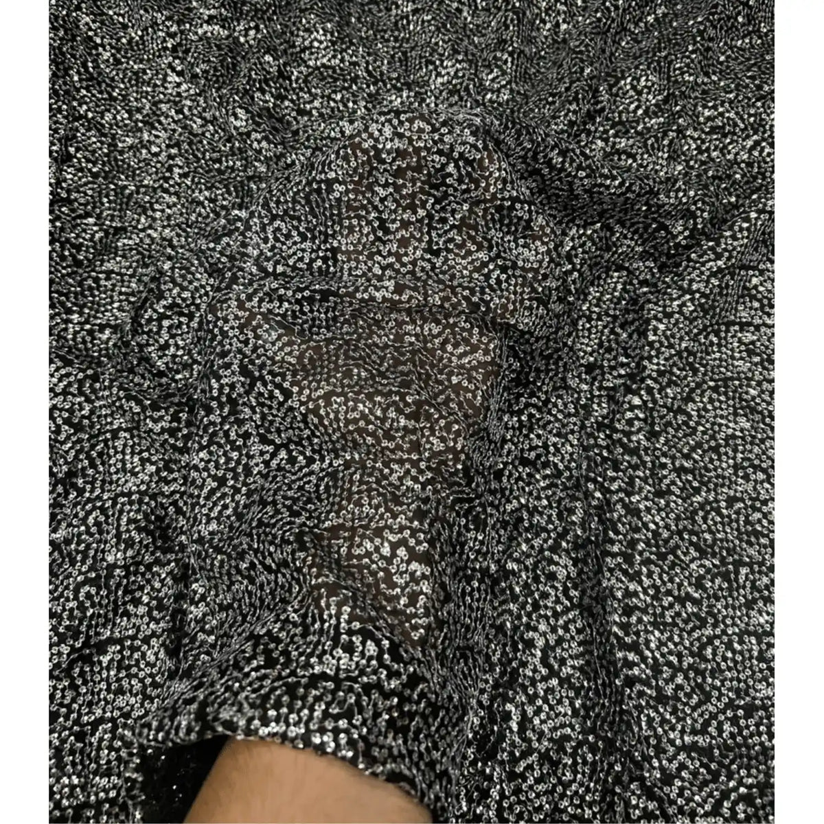 Luxury black Kichdi net fabric with dense all-over textured embroidery displayed in a spiral fold, showcasing its premium shimmer, elegant drape and rich designer finish for wedding, festive, couture and evening wear creations.