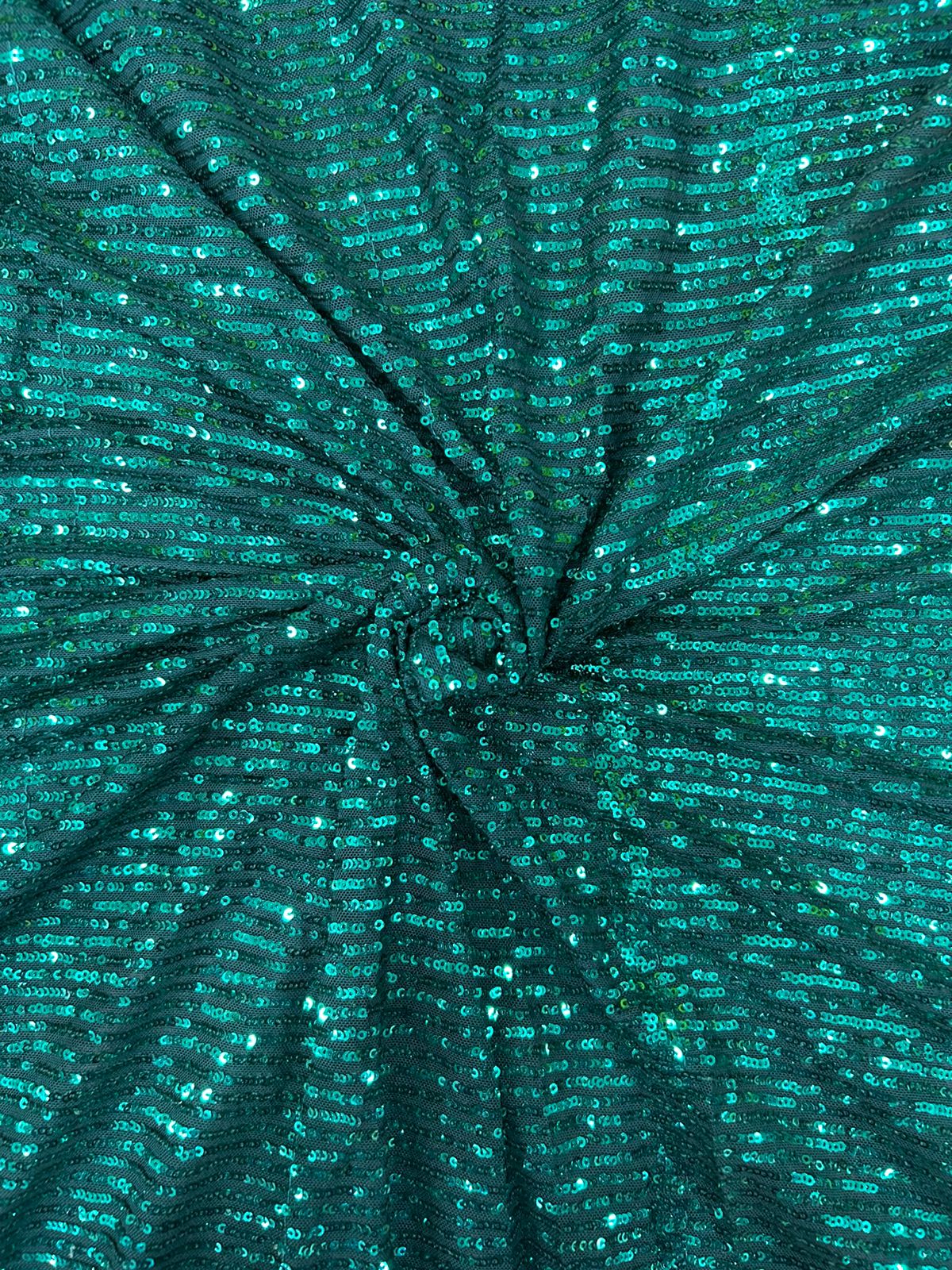 Close-up of stretchy emerald sequin net fabric, offering comfort and sparkle for custom dance costumes and designer apparel.