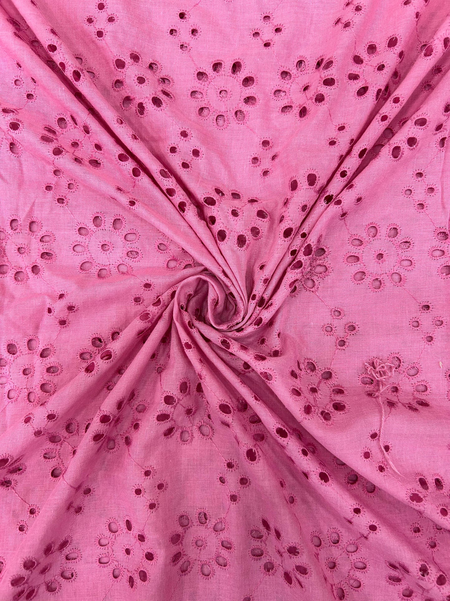 Close-up of vibrant pink cotton fabric with all-over delicate floral cutwork, perfect for comfortable summer kurtas, dresses, and fashionable outfits.