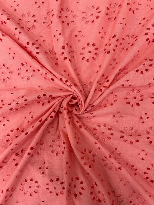 Close-up of vibrant coral pink cotton fabric with delicate floral cutwork embroidery, great for summer dresses and stylish tops.