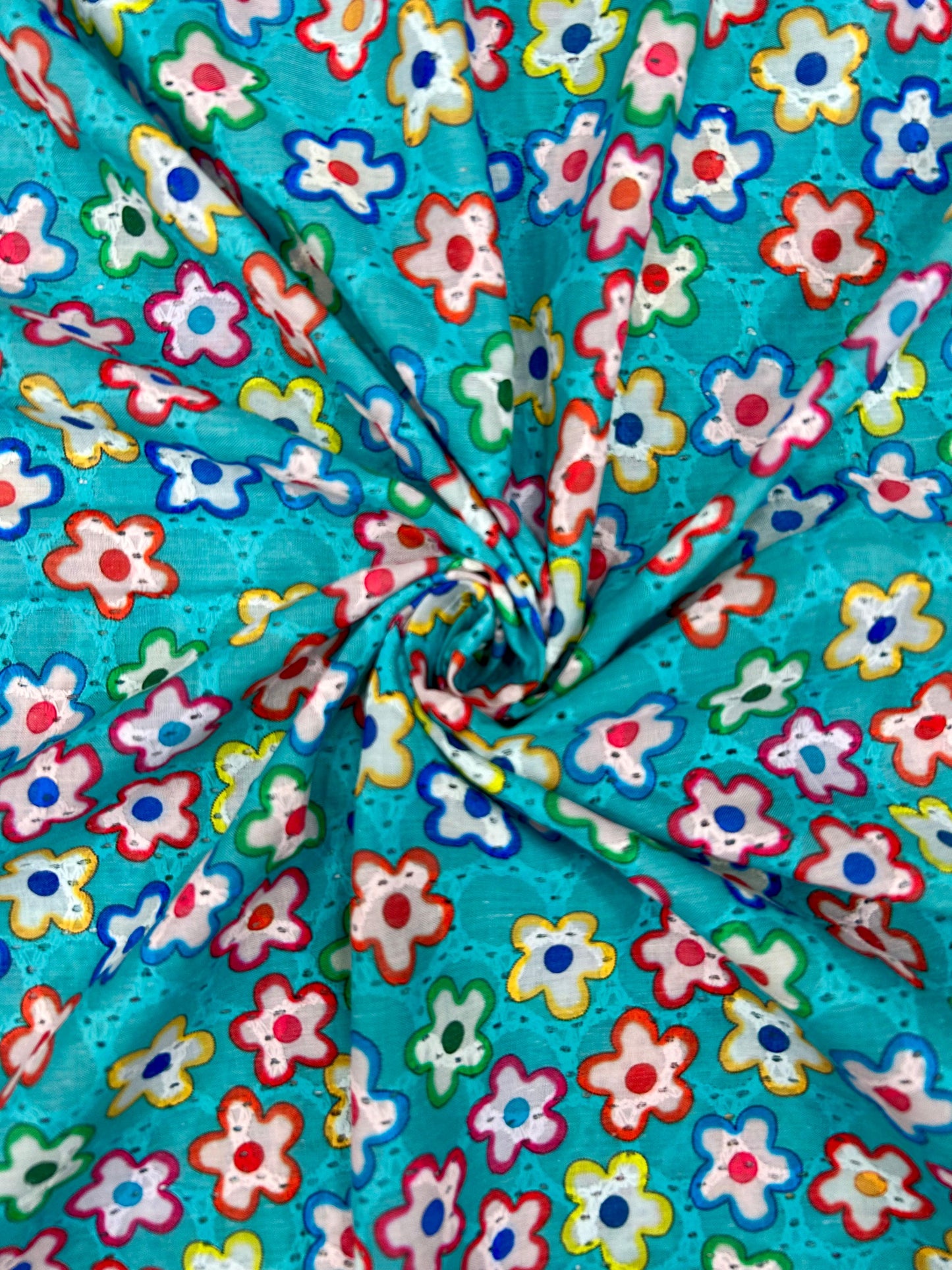 Close-up of breathable 100% cotton textile with a blue background and cheerful embroidered flower cutouts, ideal for festive and casual wear.