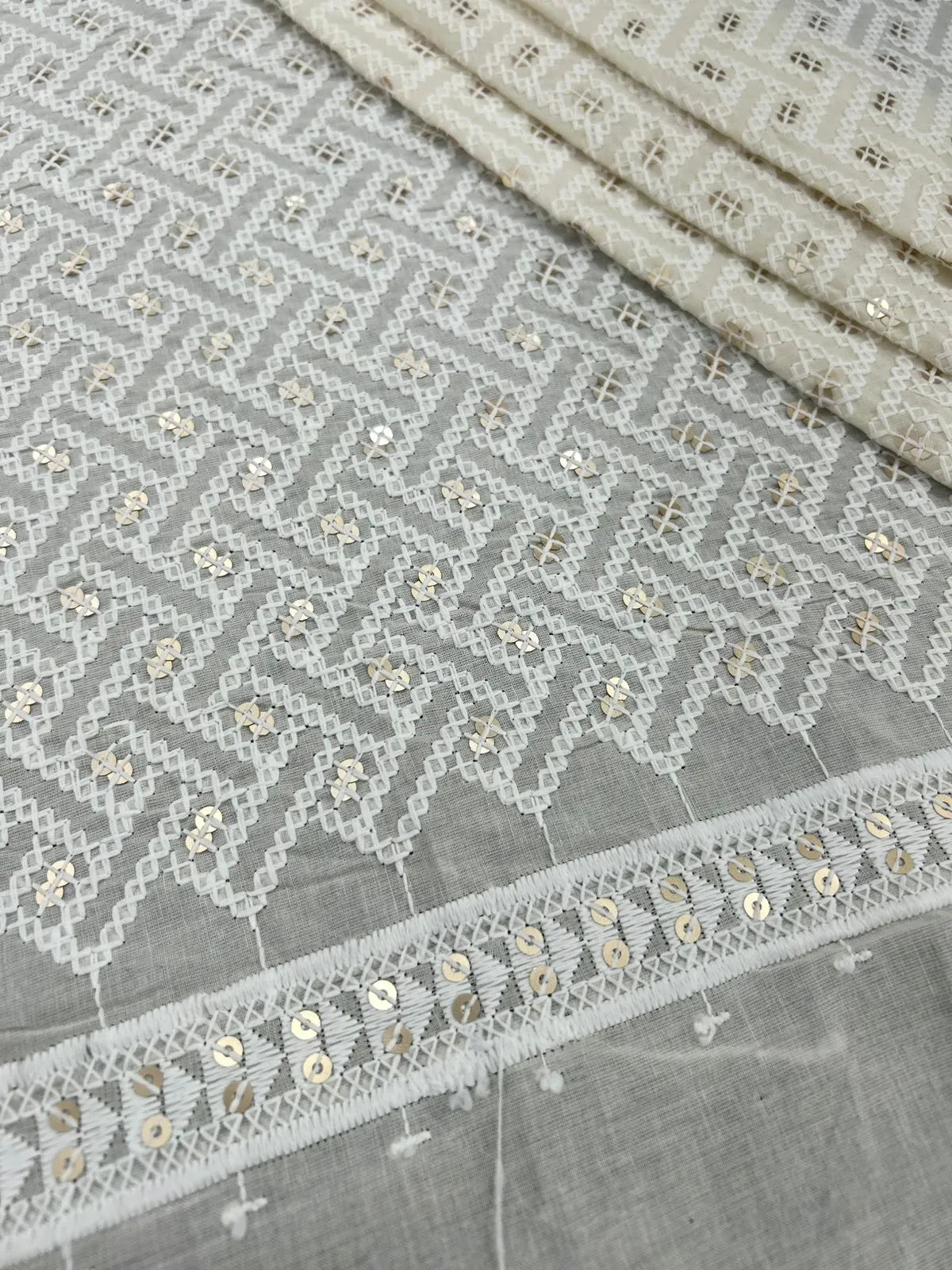 Close-up of fine thread and sequin embroidery on off-white cotton cambric fabric
