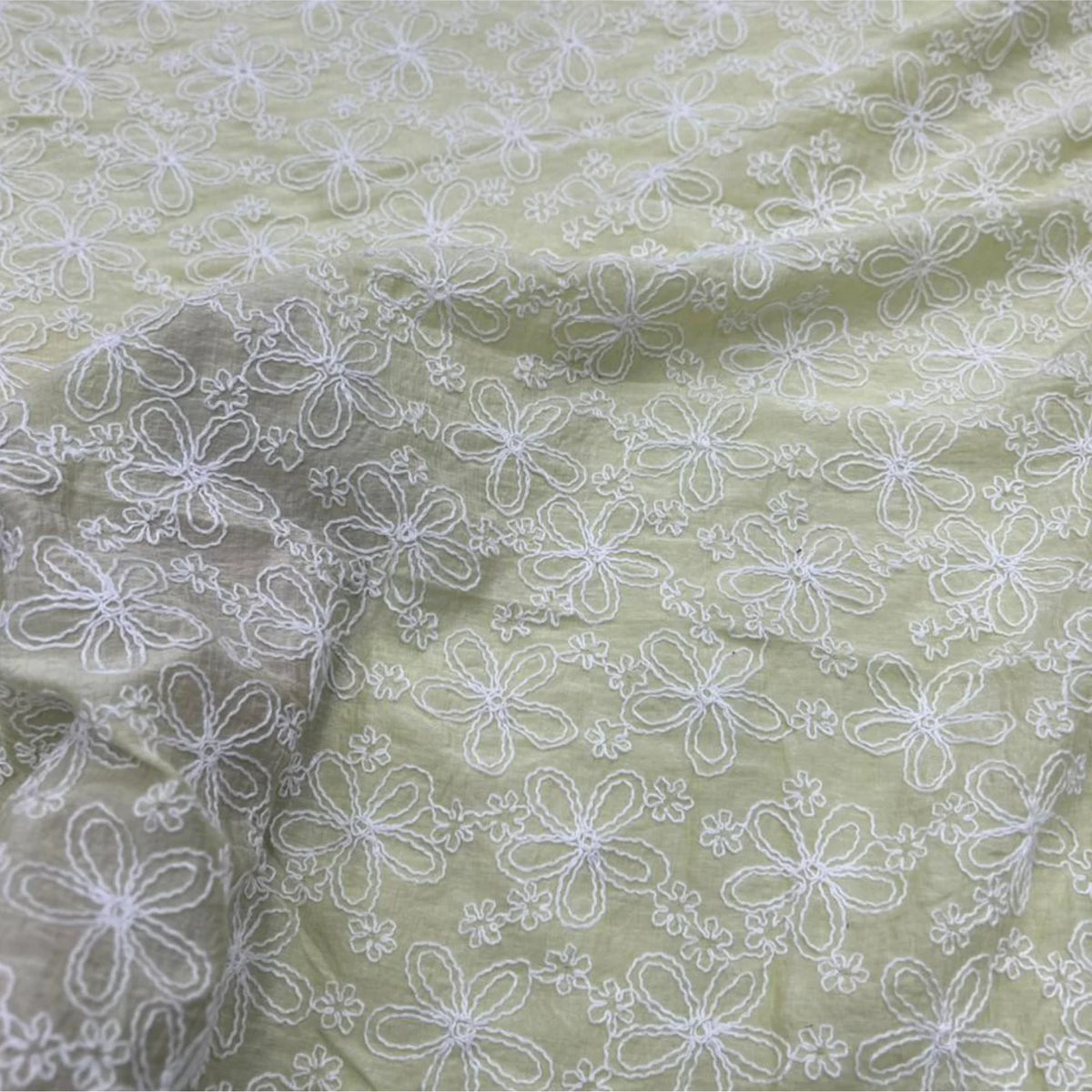 Close-up of Pastel Green Mal Chanderi fabric with white floral embroidery.