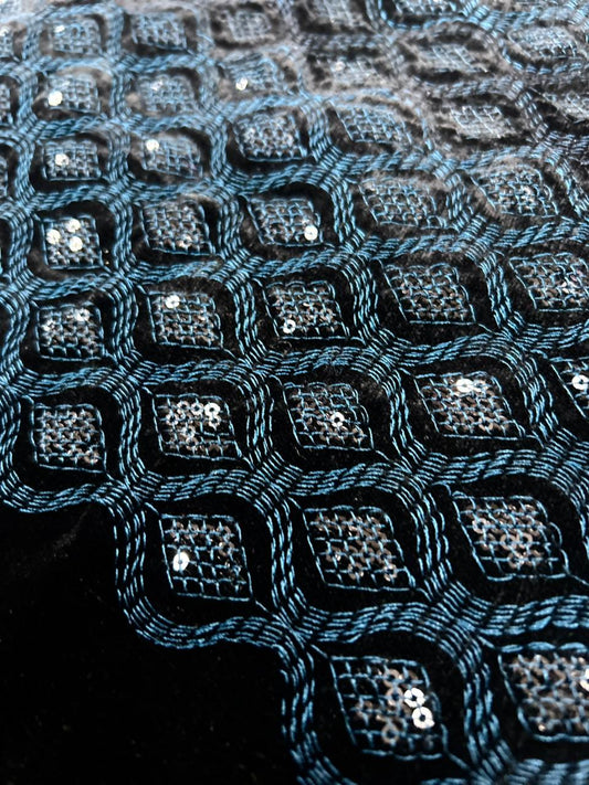 Luxury teal blue velvet fabric texture featuring dense geometric embroidery and sequins.