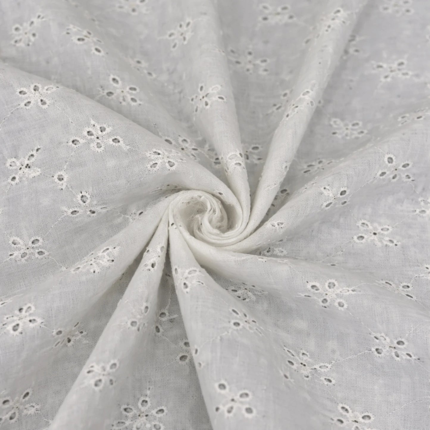 Close-up of white dyeable Hakoba Schiffli cotton fabric with floral embroidered eyelet pattern for ethnic and fashion garments.