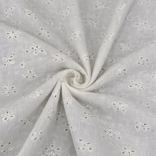 Close-up of white dyeable Hakoba Schiffli cotton fabric with floral embroidered eyelet pattern for ethnic and fashion garments.